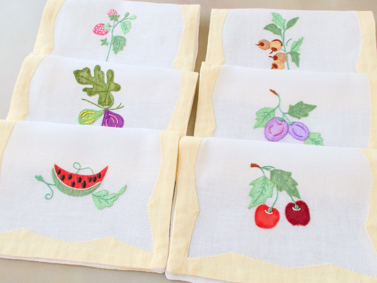 Six vintage Italian cocktail napkins fanned out showing figs, plums, cherries and watermelon embroidery designs