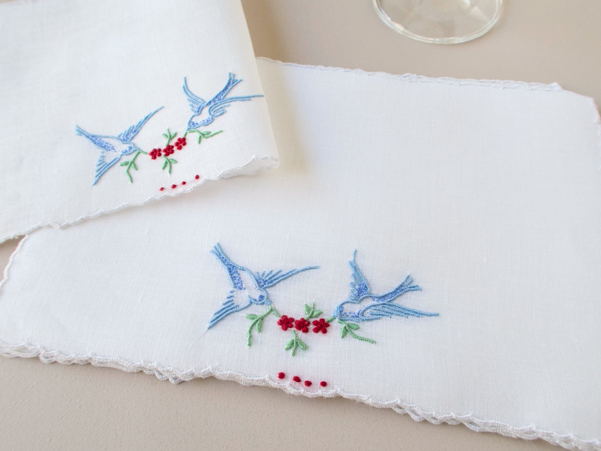 Vintage Madeira cocktail napkins stacked, white Irish linen with scalloped edges, bluebirds in flight carrying a garland of red flowers