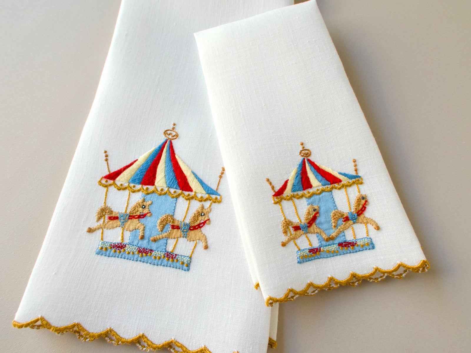 Vintage hand towel and fingertip towel displayed together, both hand embroidered in Madeira with matching carousel design in red, white, blue and gold