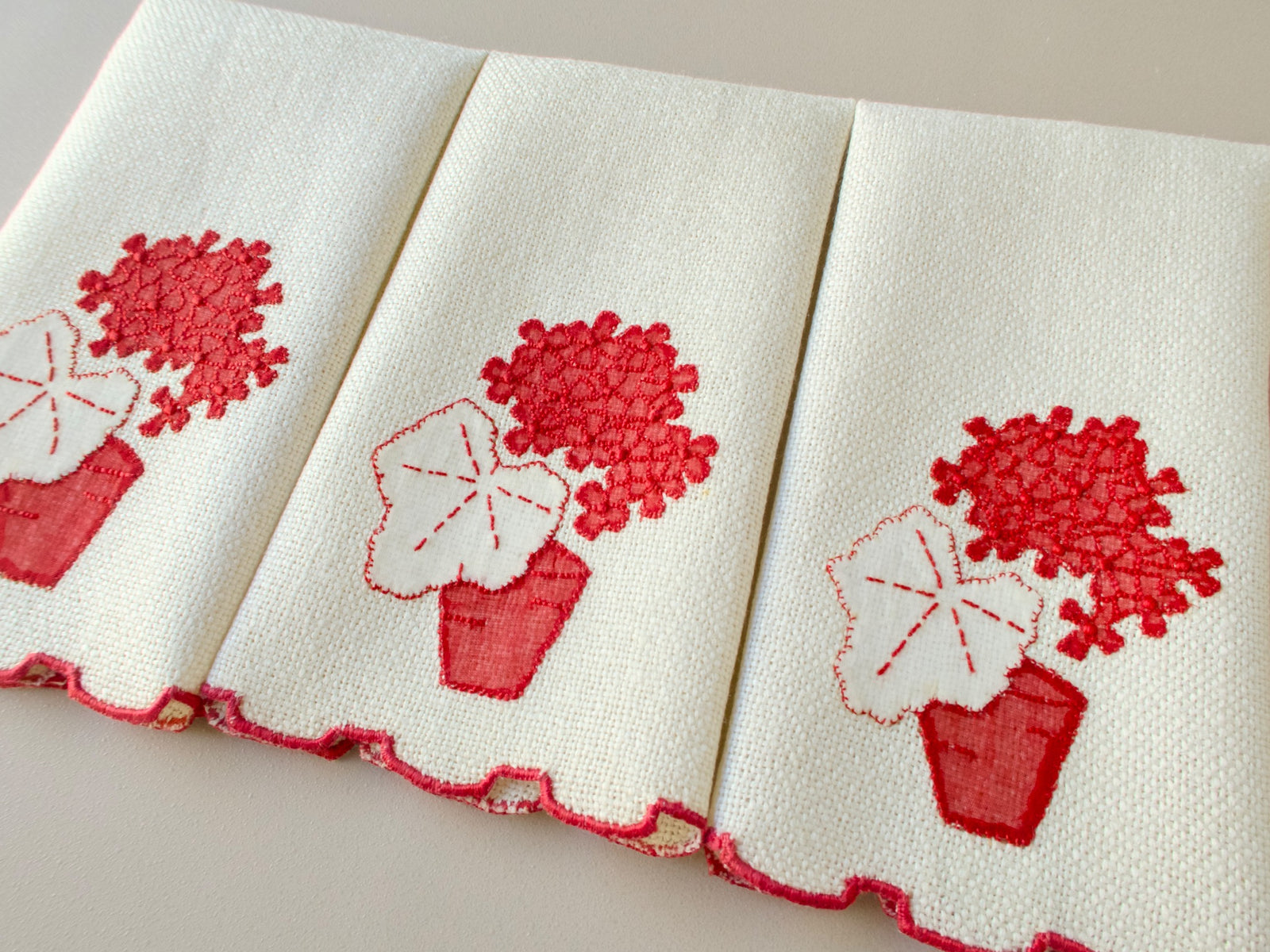 Three vintage Marghab marcasual linen fingertip towels displayed side by side showing the red “Geranium” appliqué design and stepped red hem