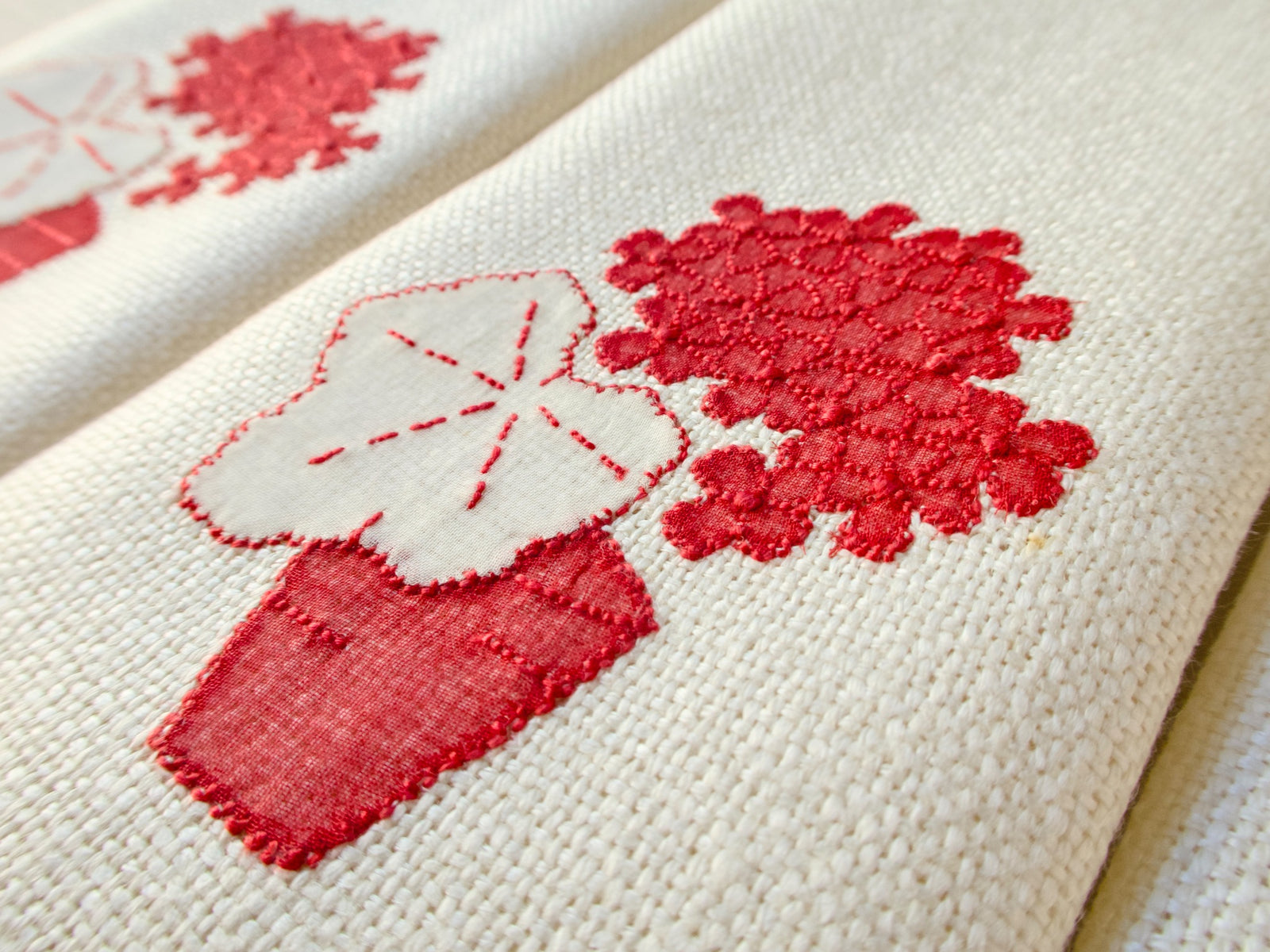 Close-up detail of vintage Marghab “Geranium” showing texture of raised red blooms above a white appliquéd geranium leaf with red vein stitching on marcasual linen