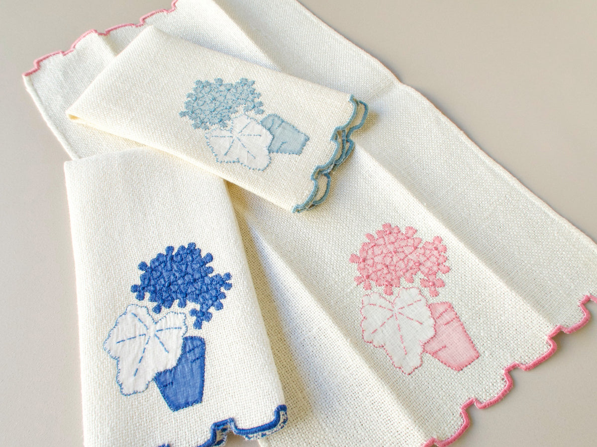 Three vintage Marghab marcasual linen “Geranium” fingertip towels spread open to show the full appliqué design in powder blue, cobalt and pink, each towel entirely in its own color​​​​​​​​​​​​​​​​