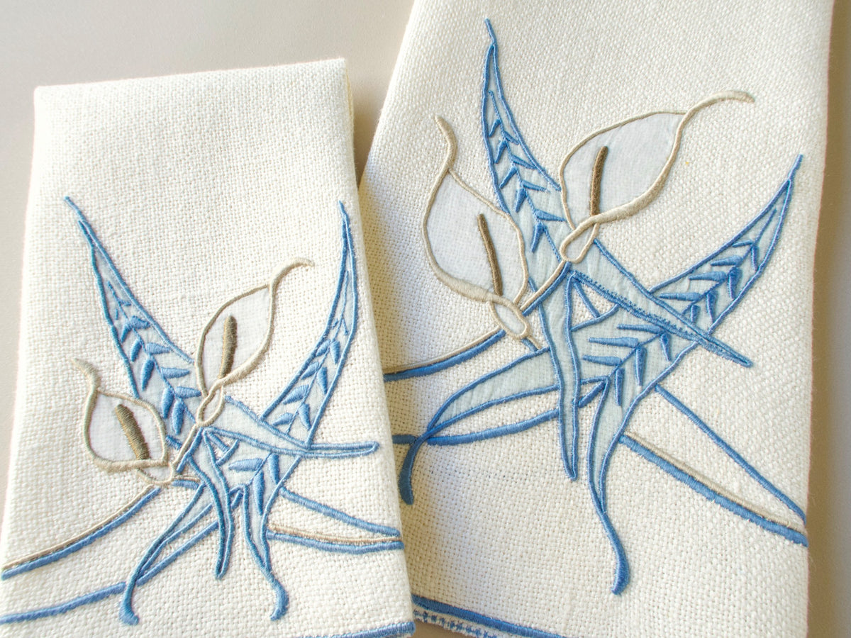 Vintage Marghab marcasual linen towels shown close up, hand embroidered with the “Calla Lily” pattern of sweeping blue fronds and white appliquéd blooms with taupe stamens