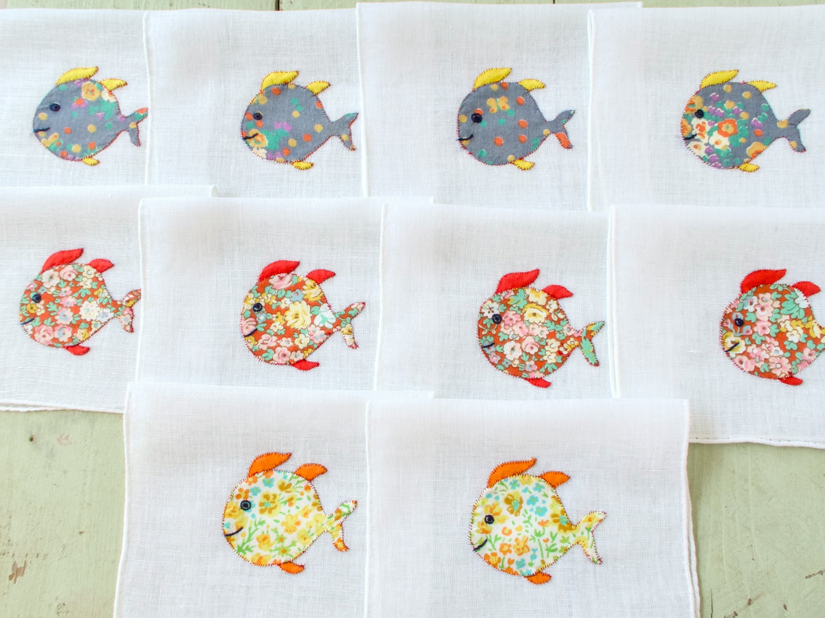 Ten vintage Italian cocktail napkins laid out in a grid showing full school of floral appliqué fish