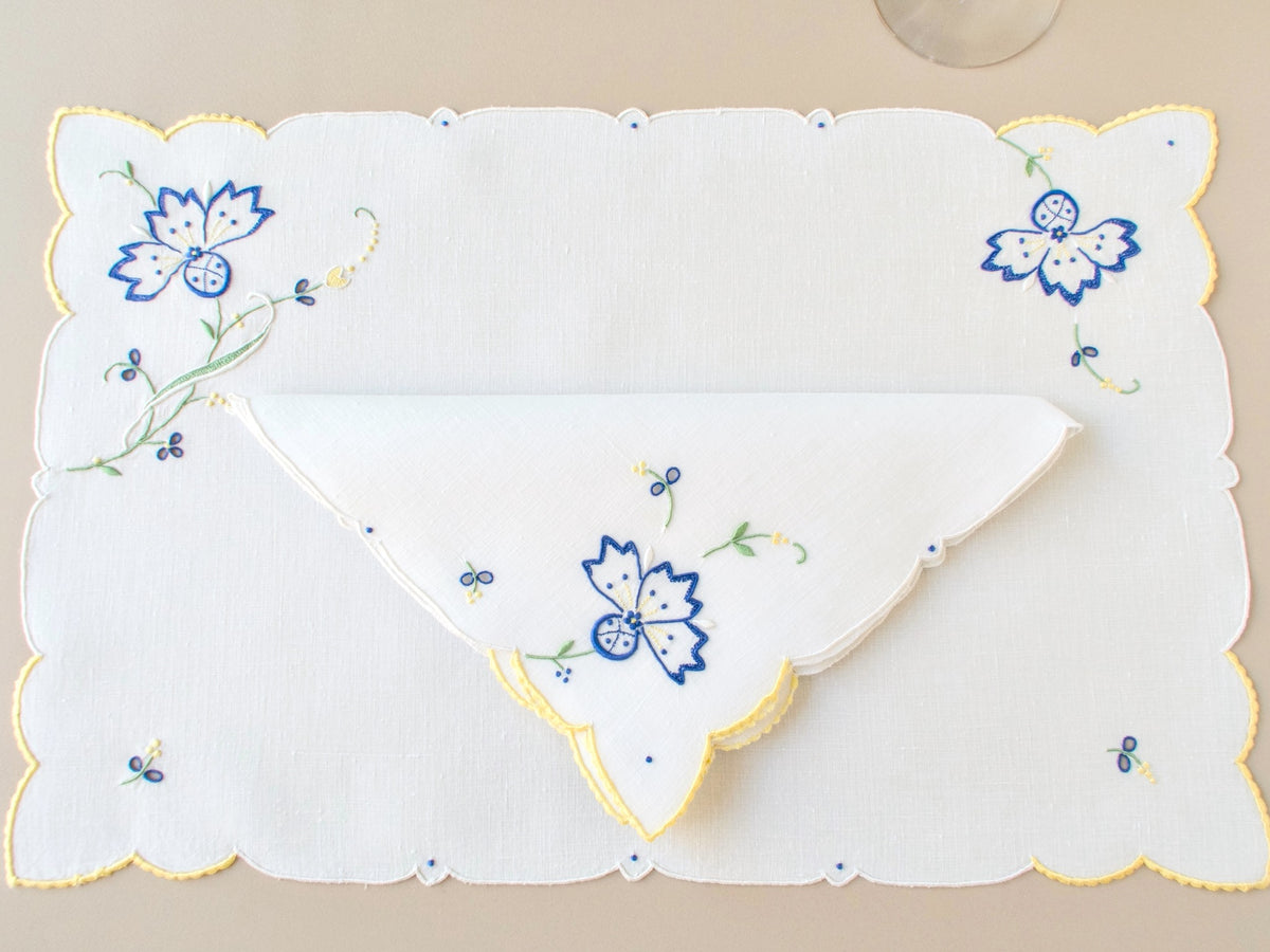 Vintage Madeira napkin folded, showing blue cornflower embroidery and yellow scalloped edge detail