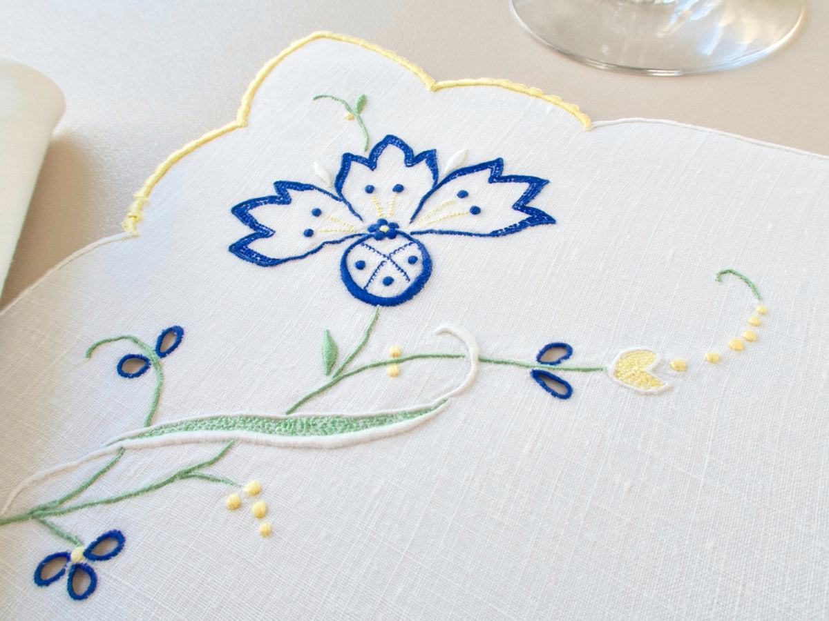 Close-up of vintage Madeira placemat showing blue cornflower embroidery with scattered blooms on white Irish linen