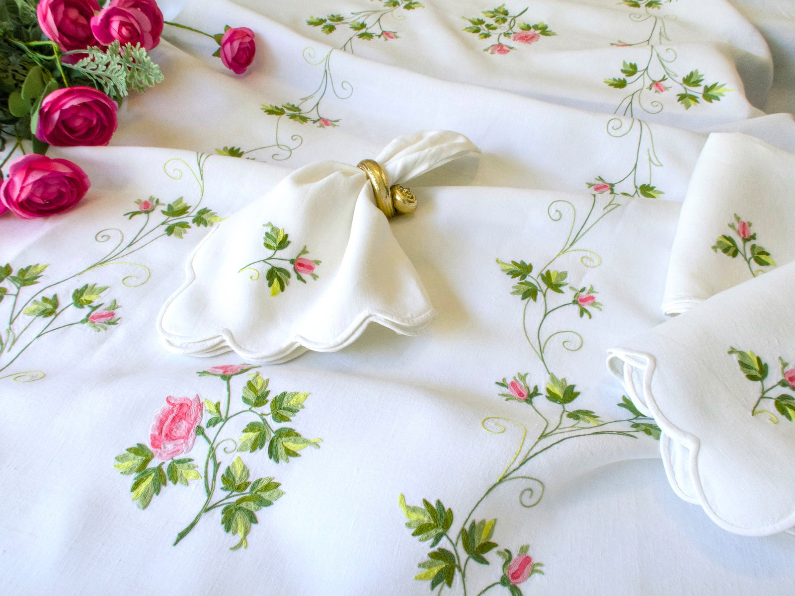 	D. Porthault tablecloth showing vining Beauvais embroidery with open rose and rosebuds, scalloped napkins with gold napkin ring