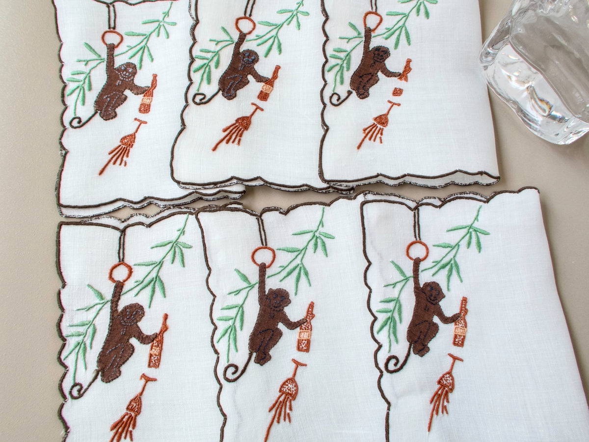 Six vintage Madeira monkey cocktail napkins arranged in two rows, white linen with dark scalloped border