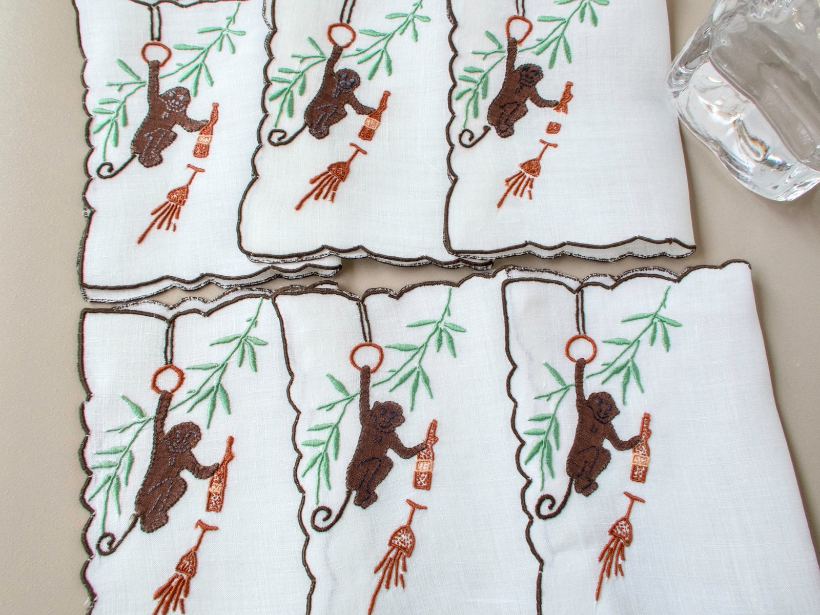Six vintage Madeira monkey cocktail napkins arranged in two rows, white linen with dark scalloped border