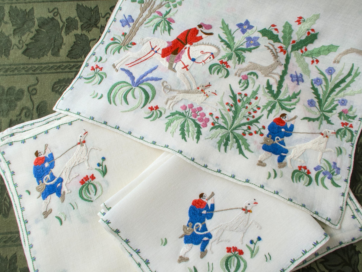 Vintage embroidered placemats and napkins with hunting scene design on a textured fabric background