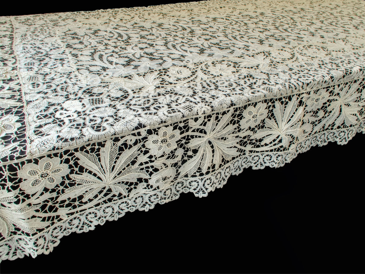 Close view of the deeply scalloped scrolling border with fan-shaped leaves and open flowers on an antique French lace tablecloth
