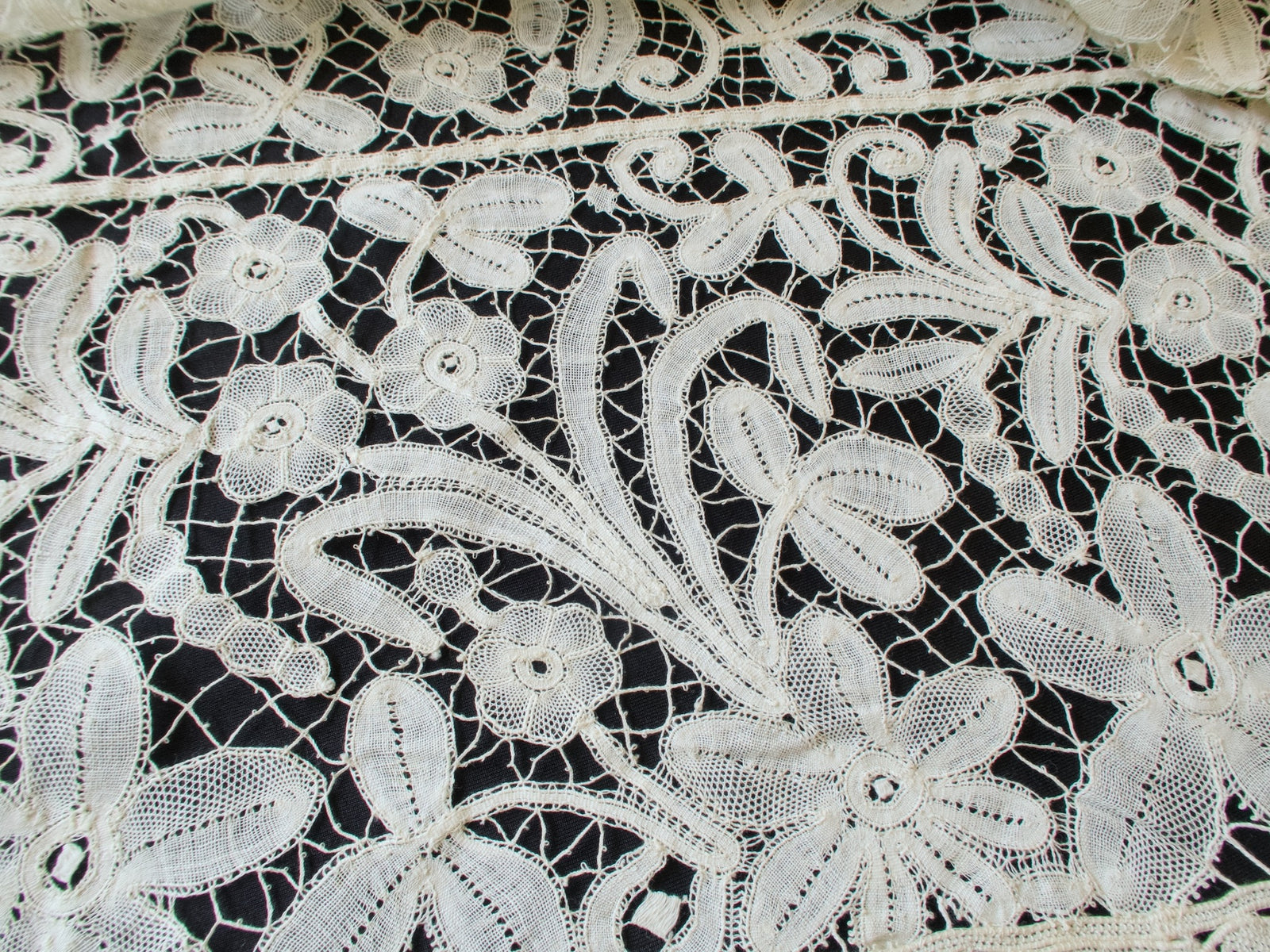 Detail of bobbin lace flowers and leaves with fine woven stitches on a net ground, antique French tablecloth