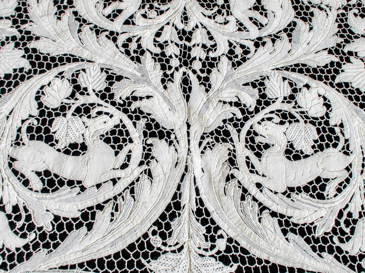 Two hounds facing each other among mirrored leaf scrolls in the lace.