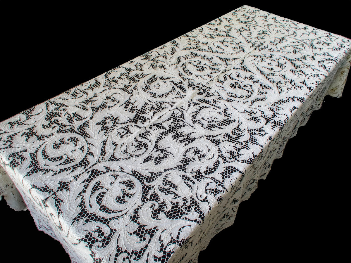 Figural lace tablecloth spread over a table, showing the patterned top and hanging sides.