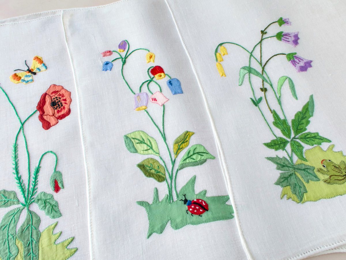 Three vintage Italian hand embroidered linen placemats showing colorful flowers with ladybug and botanical detail on semi-sheer linen