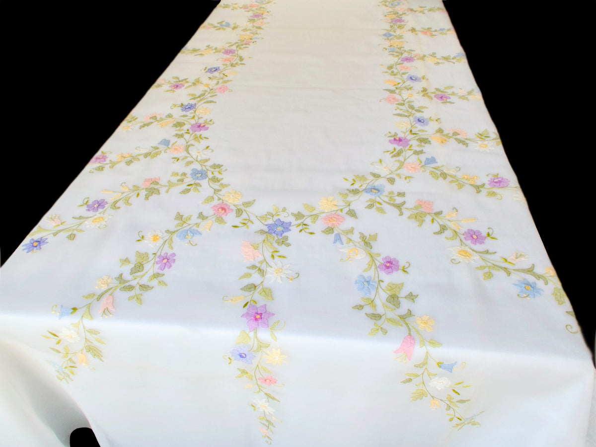 Overhead view of a vintage hand-embroidered organdy tablecloth with pastel floral garlands