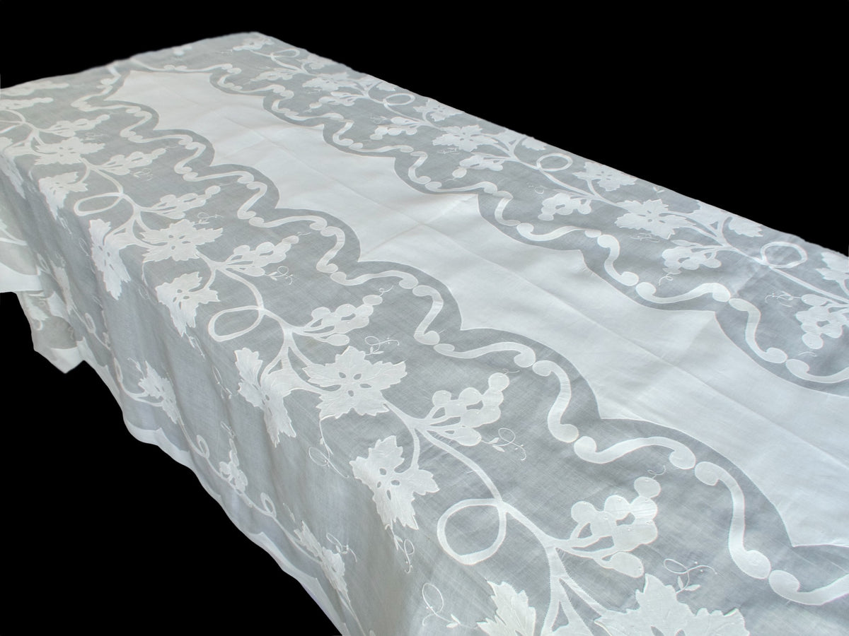 Long organdy tablecloth draped over a table, showing its sheer embroidered border and plain white center.