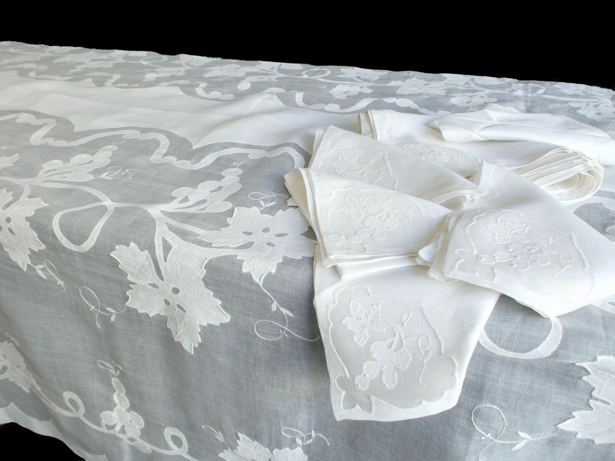 Vintage Madeira organdy tablecloth with white grape and leaf embroidery, shown with folded napkins against a dark background.