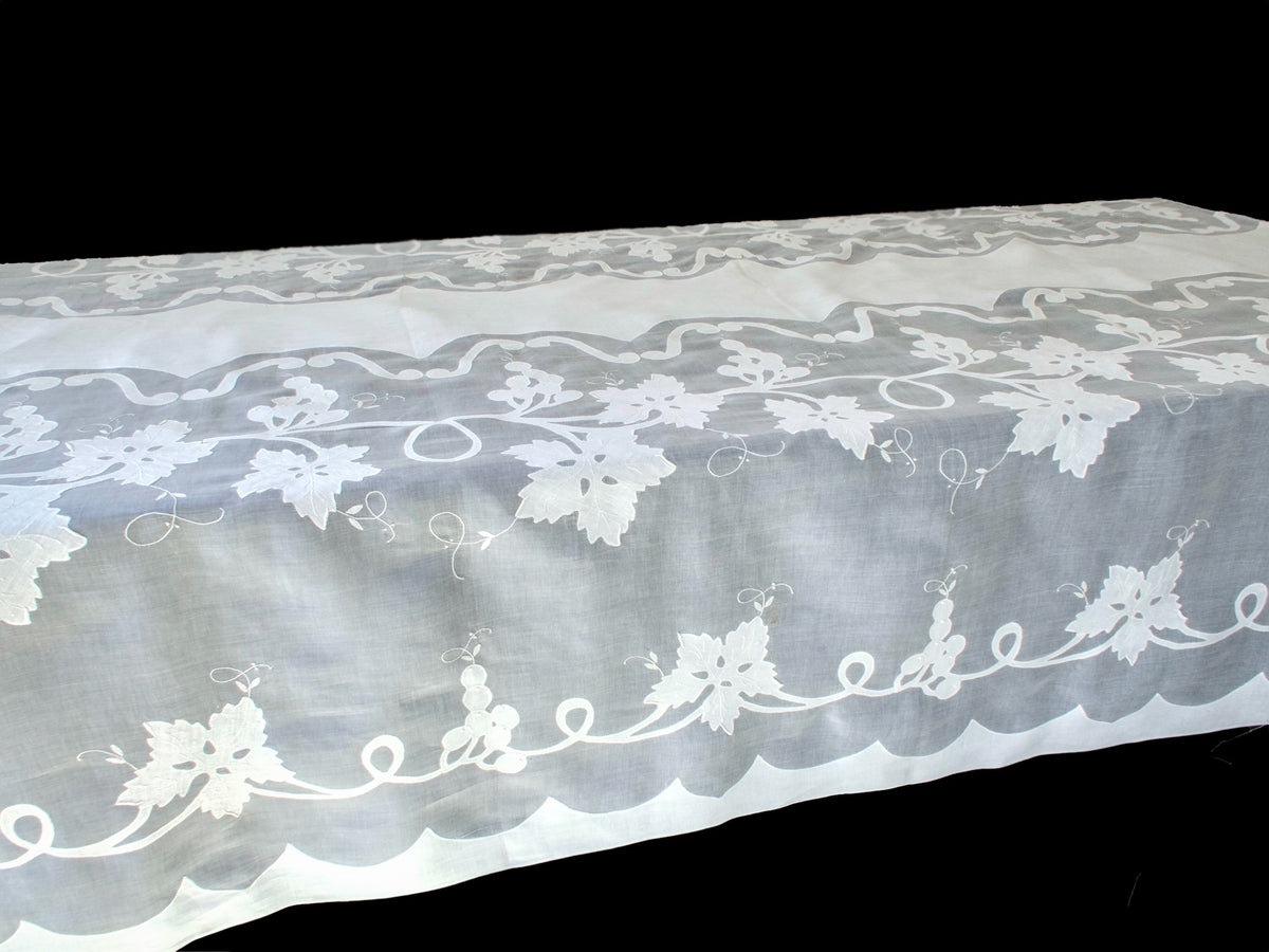 Long organdy tablecloth draped over a table, showing its sheer embroidered border and plain white center.