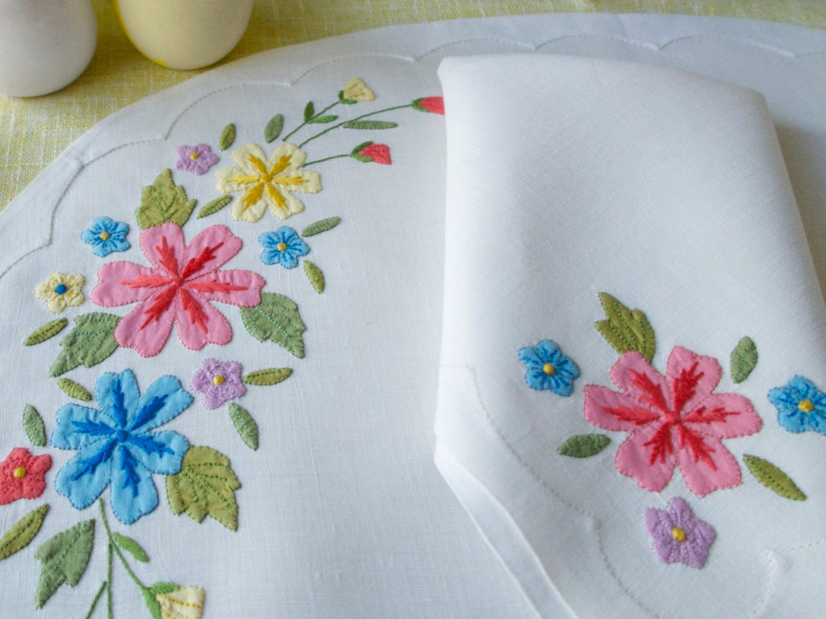 Vintage Madeira linen placemat and napkin set with bright hand-embroidered flowers in pink, blue, and yellow on white linen.
