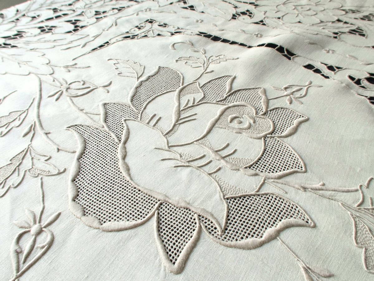 Detail of hand-embroidered roses with padded satin stitches and cutwork on ecru linen.