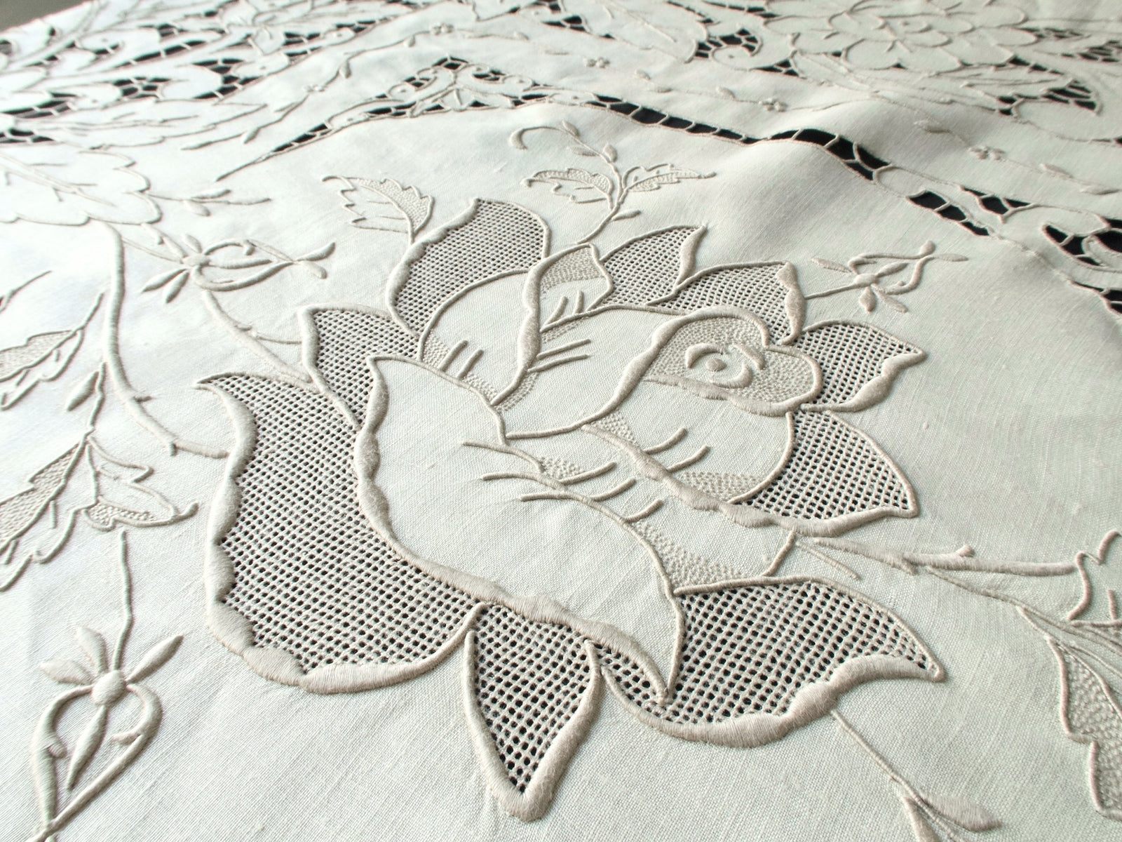 Detail of hand-embroidered roses with padded satin stitches and cutwork on ecru linen.