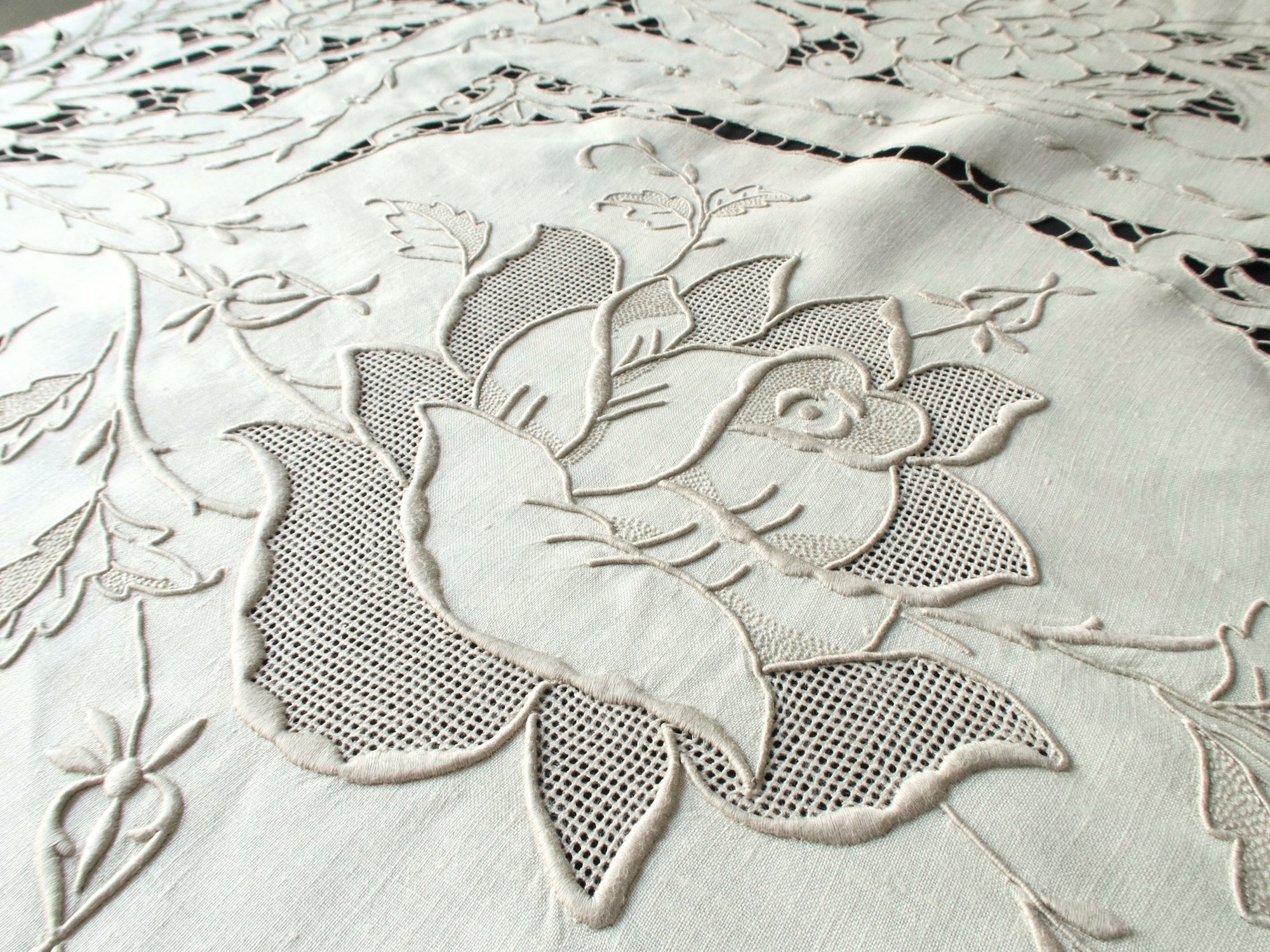 Detail of hand-embroidered roses with padded satin stitches and cutwork on ecru linen.