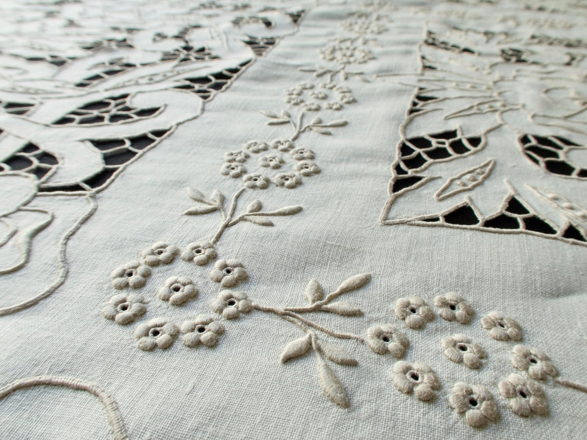 Close-up of cutwork and padded satin stitches on handmade Madeira tablecloth, showing intricate floral motifs and raised texture.