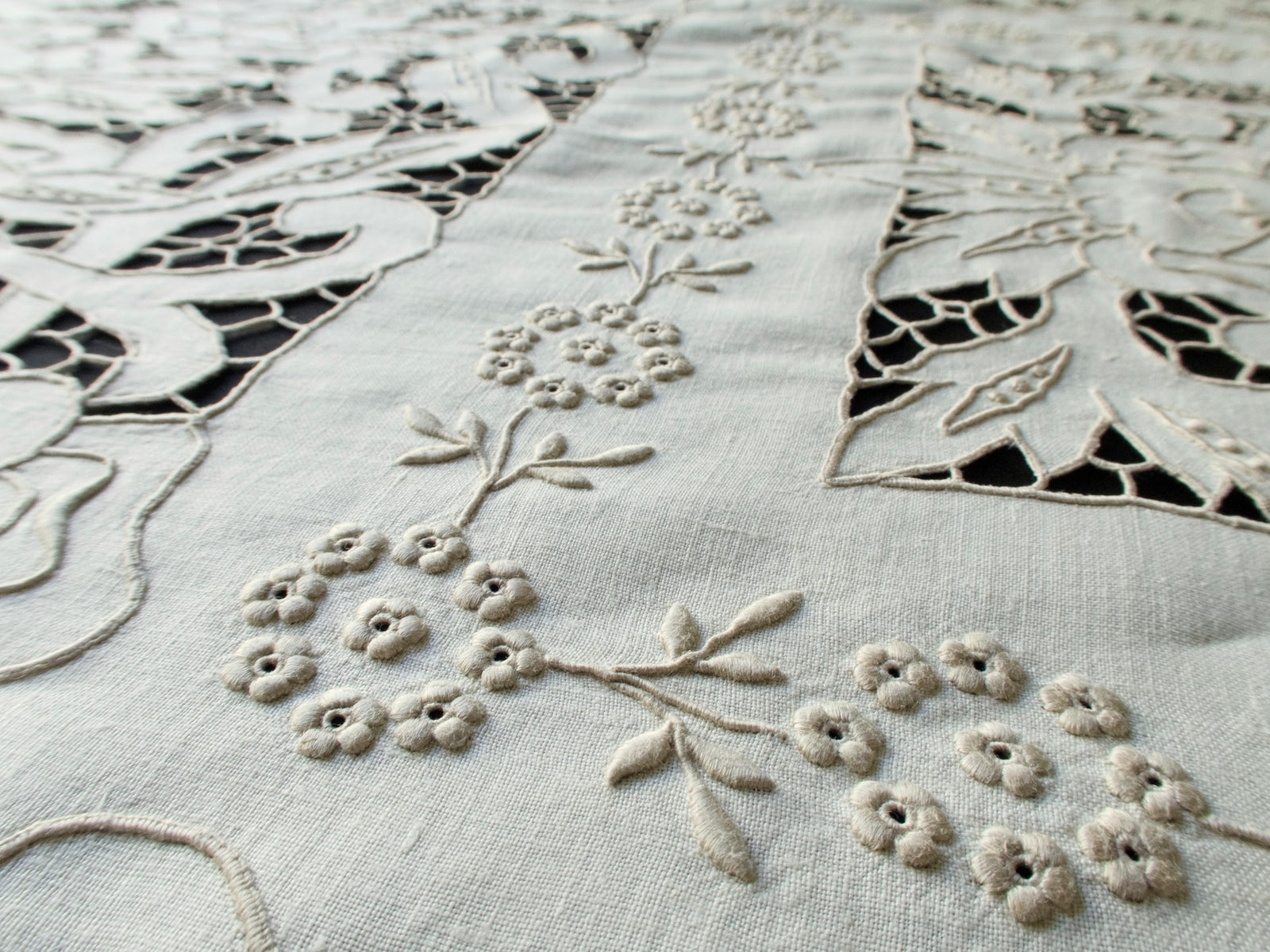 Close-up of cutwork and padded satin stitches on handmade Madeira tablecloth, showing intricate floral motifs and raised texture.