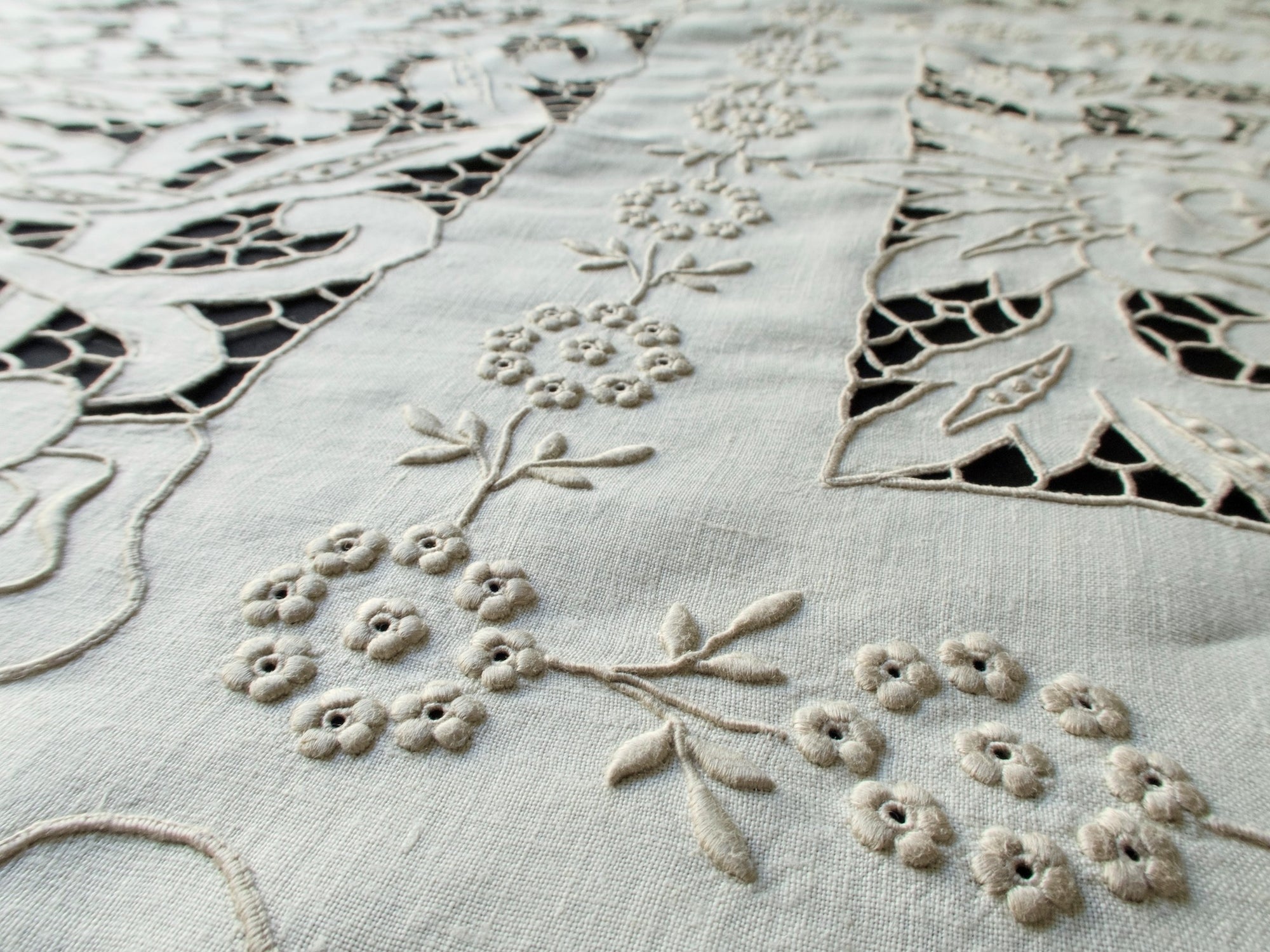 Close-up of cutwork and padded satin stitches on handmade Madeira tablecloth, showing intricate floral motifs and raised texture.