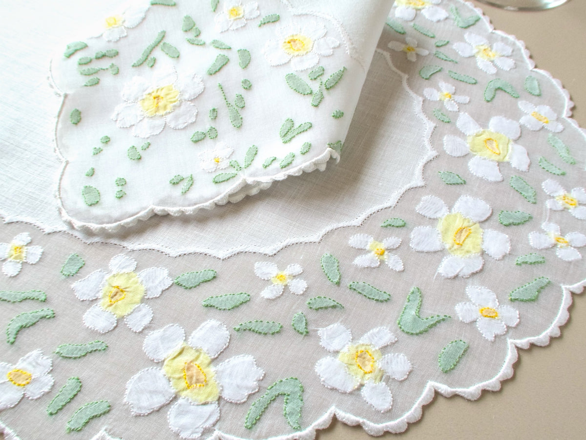 Close-up of vintage Madeira organdy placemat border showing white appliquéd daisies with yellow centers against sheer organdy and linen center