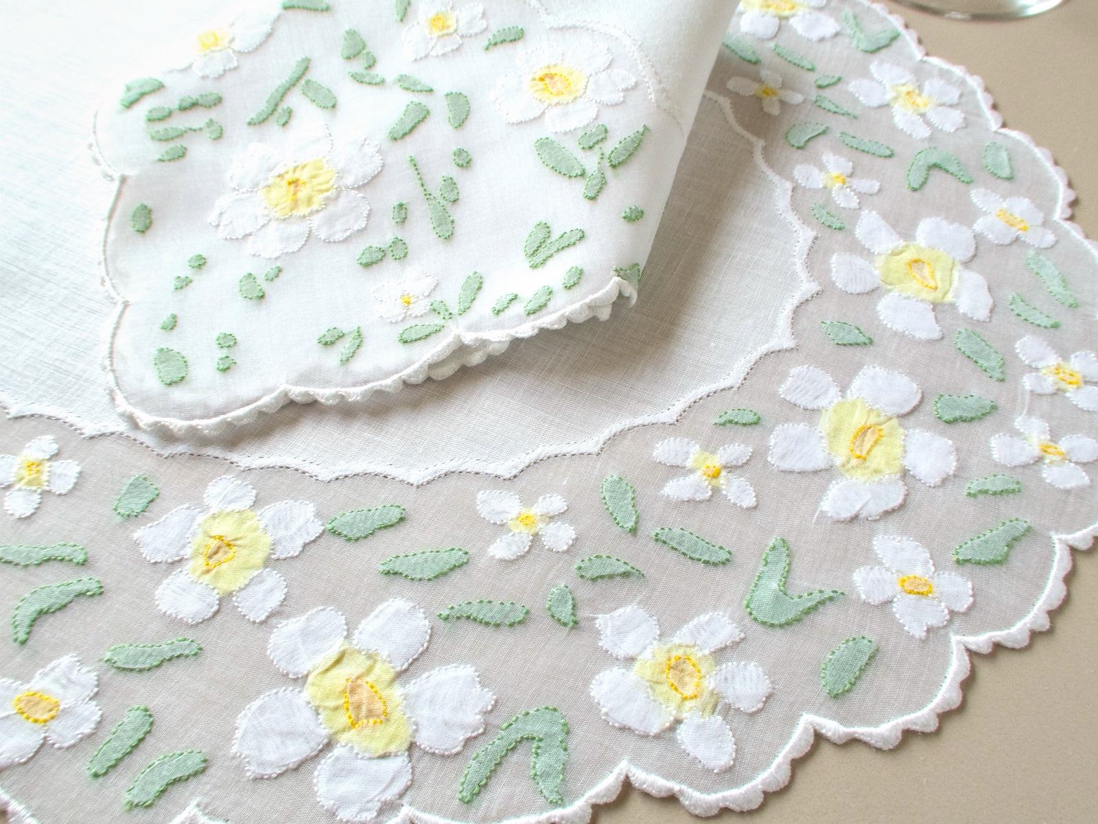 Close-up of vintage Madeira organdy placemat border showing white appliquéd daisies with yellow centers against sheer organdy and linen center