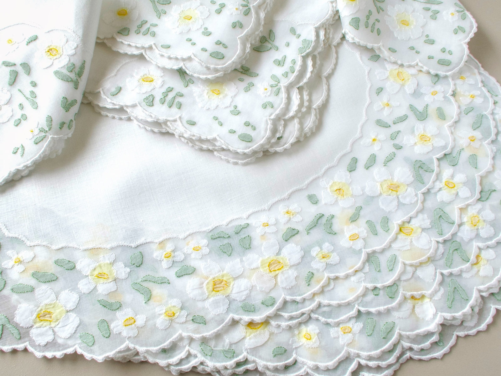 Stack of eight vintage Madeira napkins with white appliquéd daisies and scalloped borders showing full set