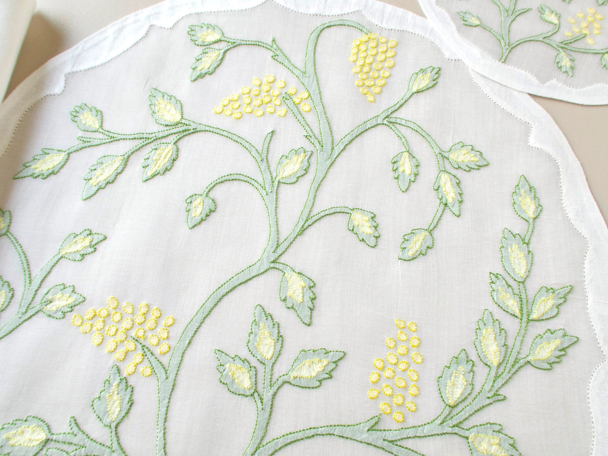 Overhead close-up of vintage Madeira organdy placemat showing full Jacobean vine and leaf shadow work embroidery pattern in sage green with yellow flower clusters