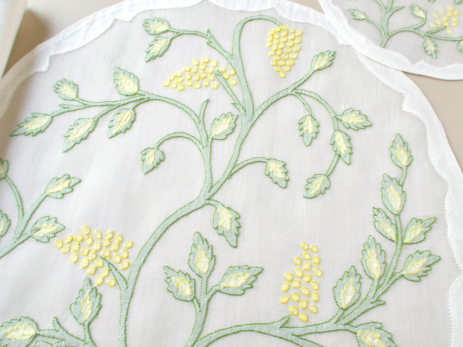 Overhead close-up of vintage Madeira organdy placemat showing full Jacobean vine and leaf shadow work embroidery pattern in sage green with yellow flower clusters