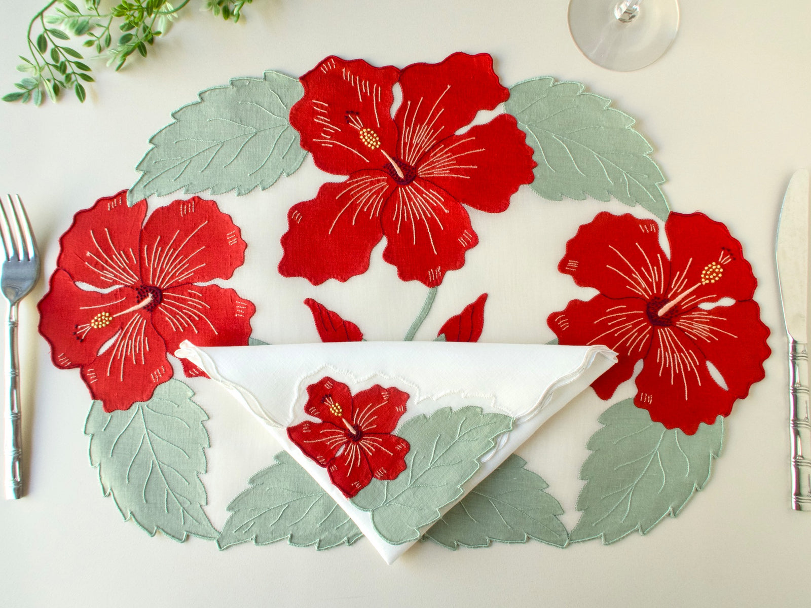 Overhead view of vintage Madeira organdy placemat with linen appliqué hibiscus and matching napkin, silver cutlery on beige background