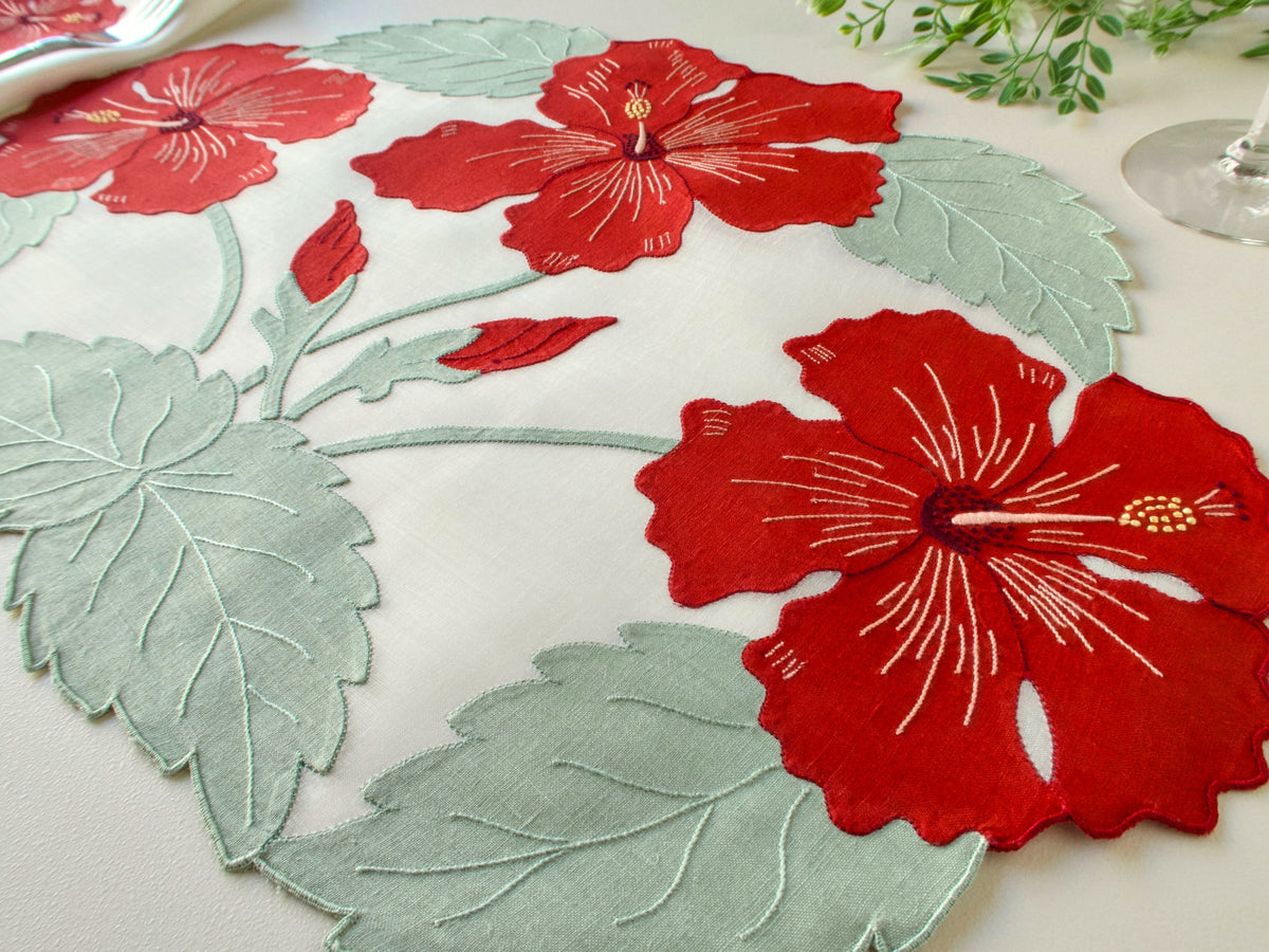 Close-up angled view of vintage Madeira organdy placemat with linen appliqué red hibiscus blooms and sage green leaves