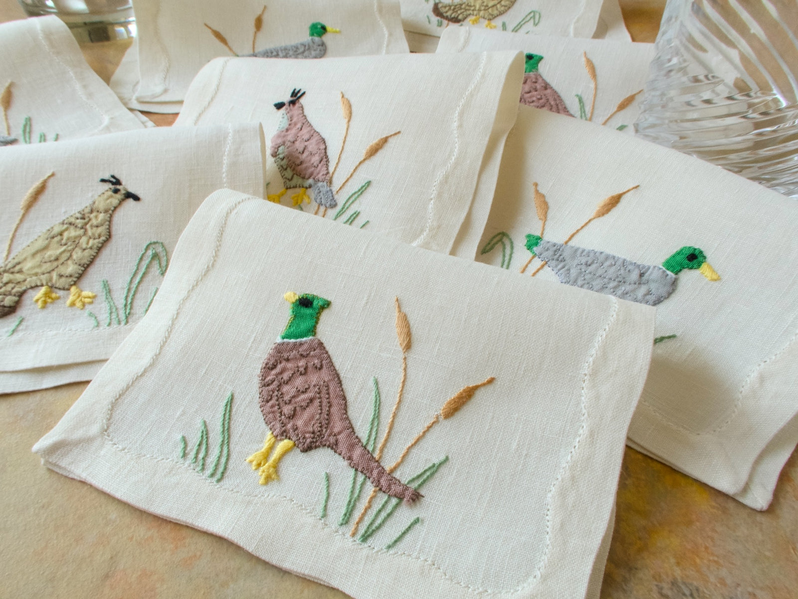 Set of embroidered napkins with bird designs on a wooden surface