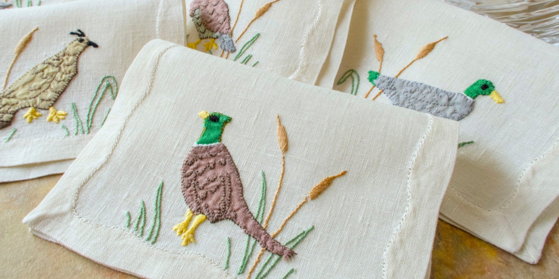 Set of vintage embroidered Madeira linen cocktail napkins with bird designs on a wooden surface