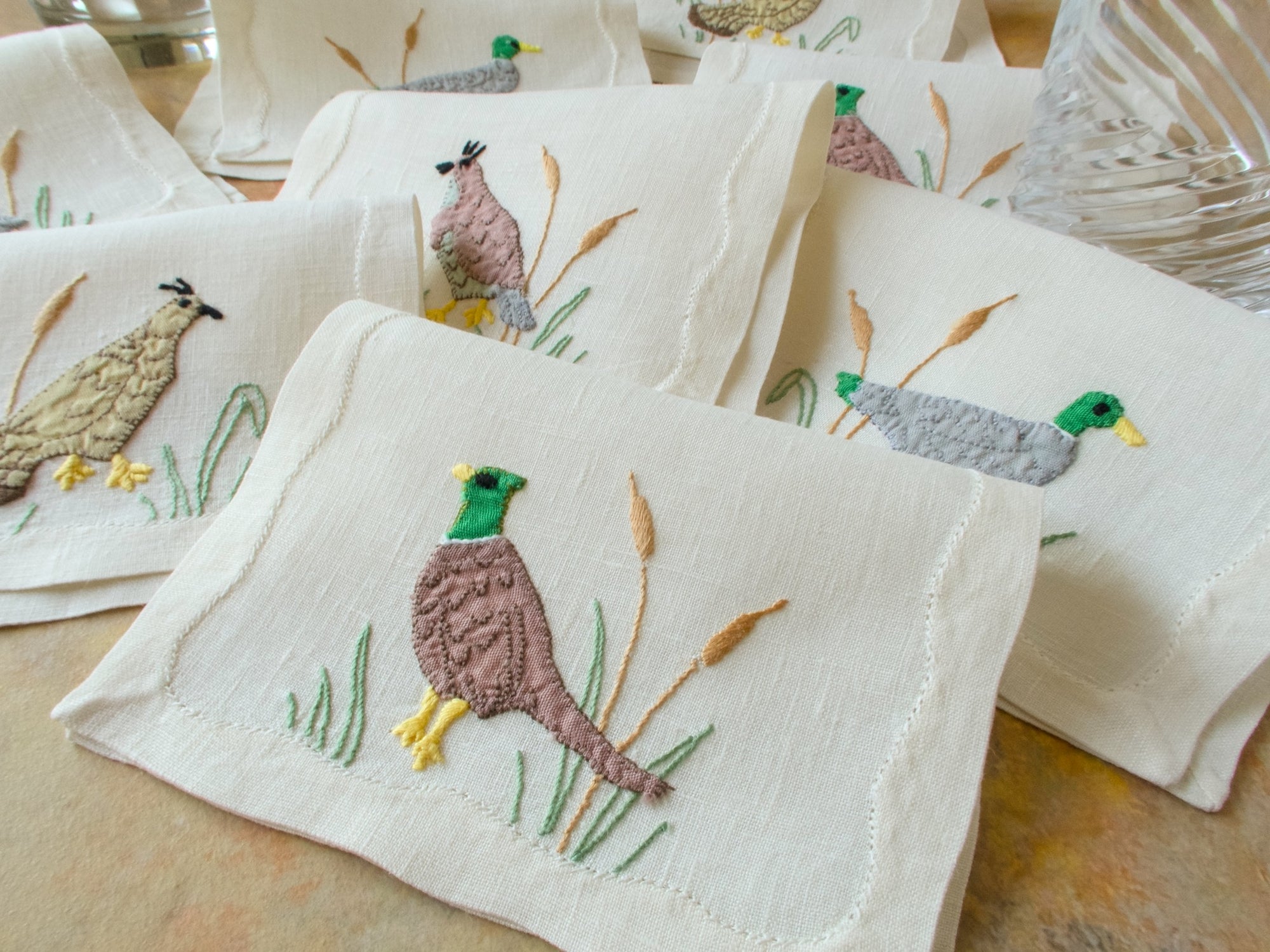 Set of embroidered napkins with bird designs on a wooden surface
