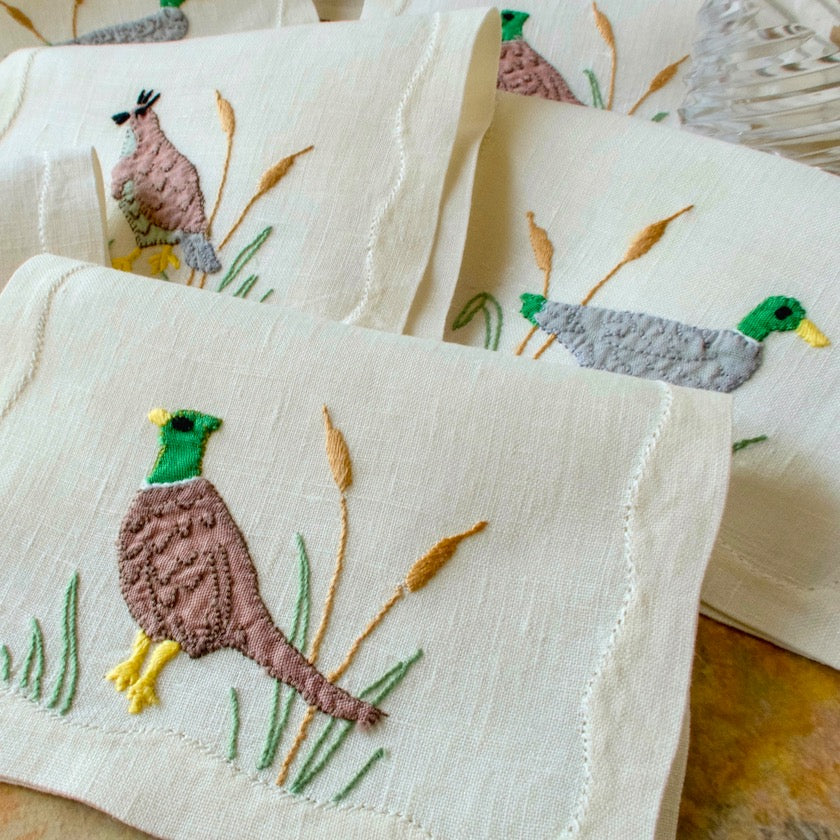 Set of vintage embroidered Madeira linen cocktail napkins with bird designs on a wooden surface