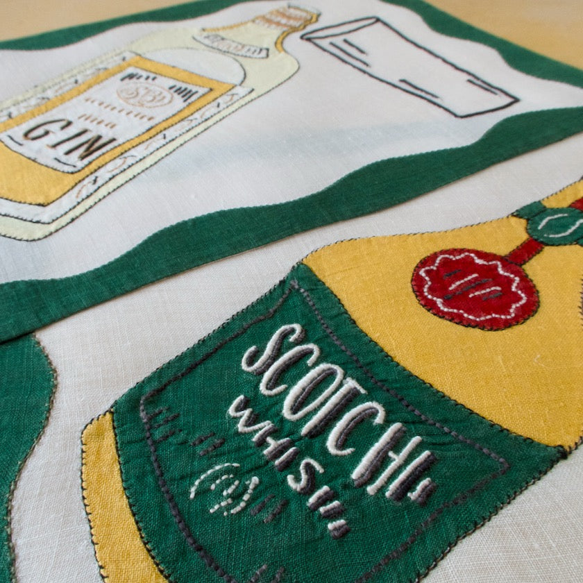 Embroidered design of a bottle labeled 'Gin' and another labeled 'Scotch Whisky' on fabric, vintage cocktail napkins from Madeira