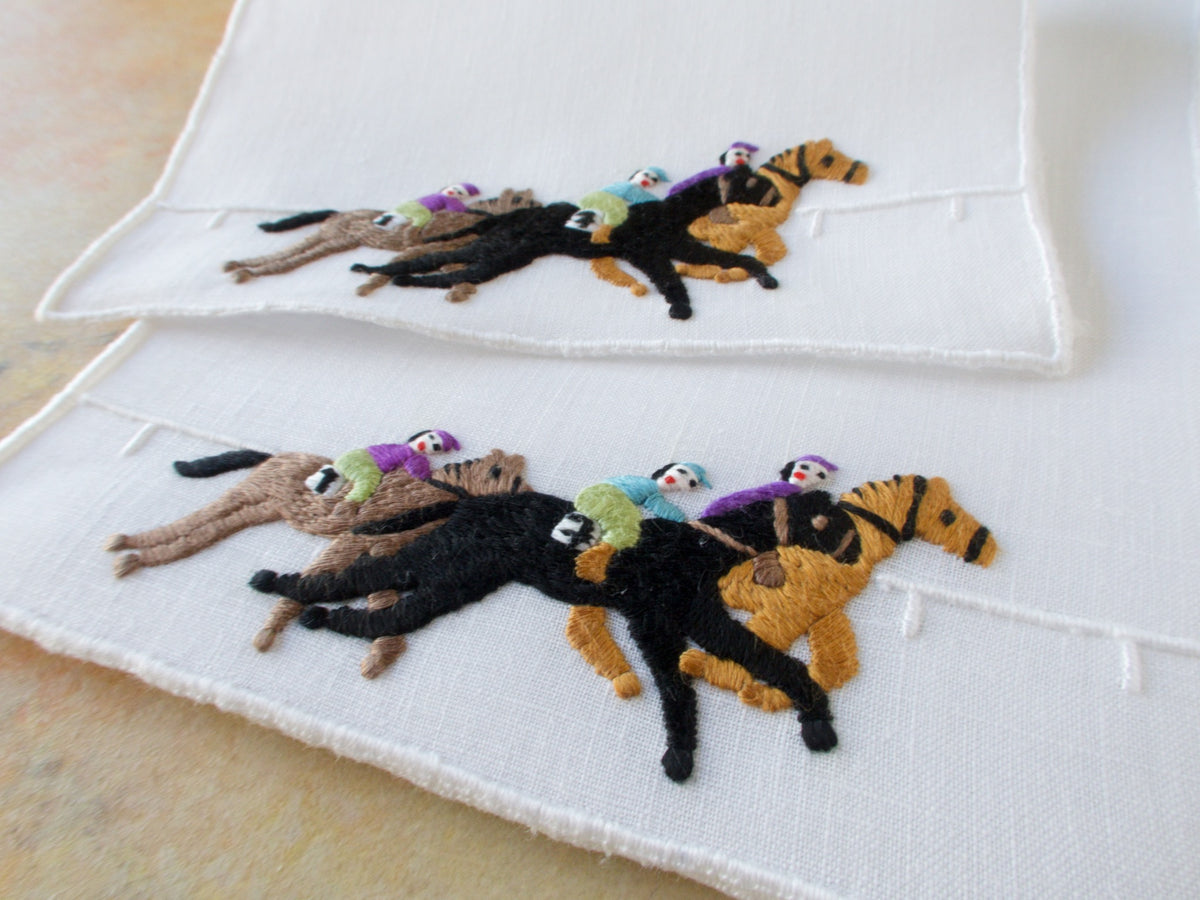 Close view of two vintage Madeira cocktail napkins with hand embroidered racehorses and jockeys in motion