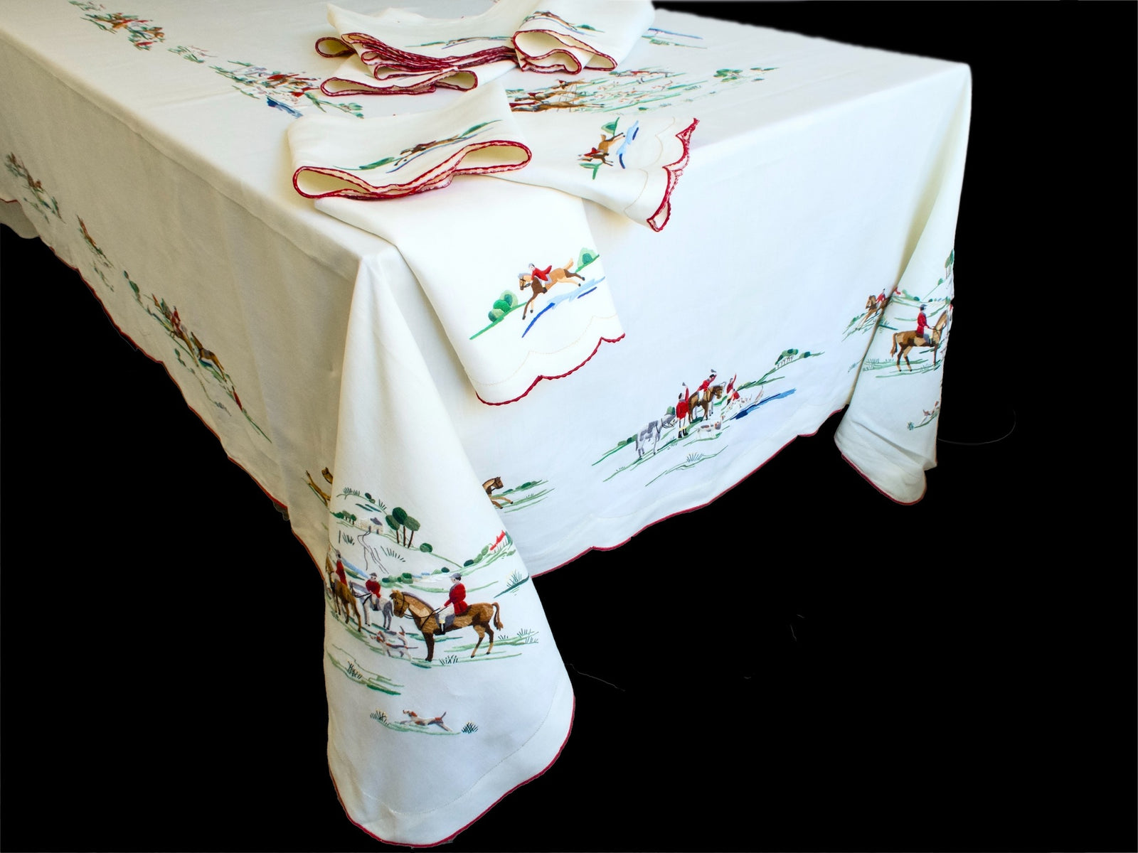 Vintage Madeira fox hunt tablecloth draped over a table corner with scalloped red-edged napkins stacked on top