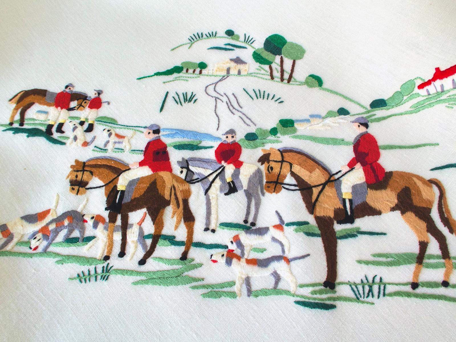 Three red-coated riders on horseback with hounds and a hilltop farmhouse hand embroidered on vintage Madeira linen