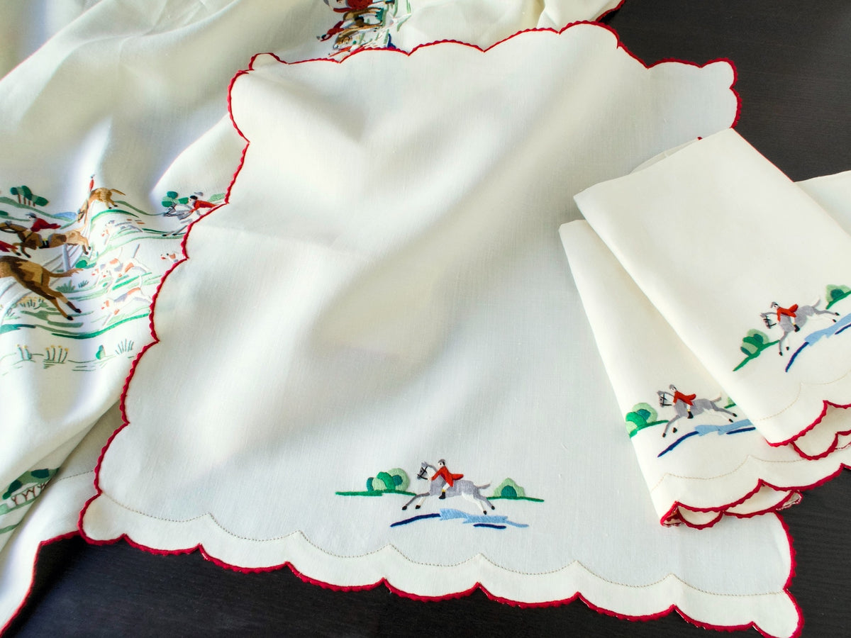 Vintage Madeira napkin with a scalloped red edge and a hand embroidered rider on a grey horse leaping a stream