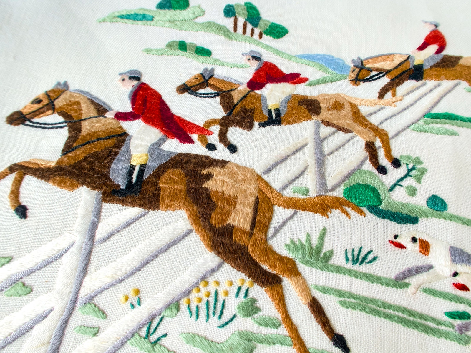 Vintage Madeira tablecloth with hand embroidered red-coated riders on galloping horses clearing a white fence, hounds racing below