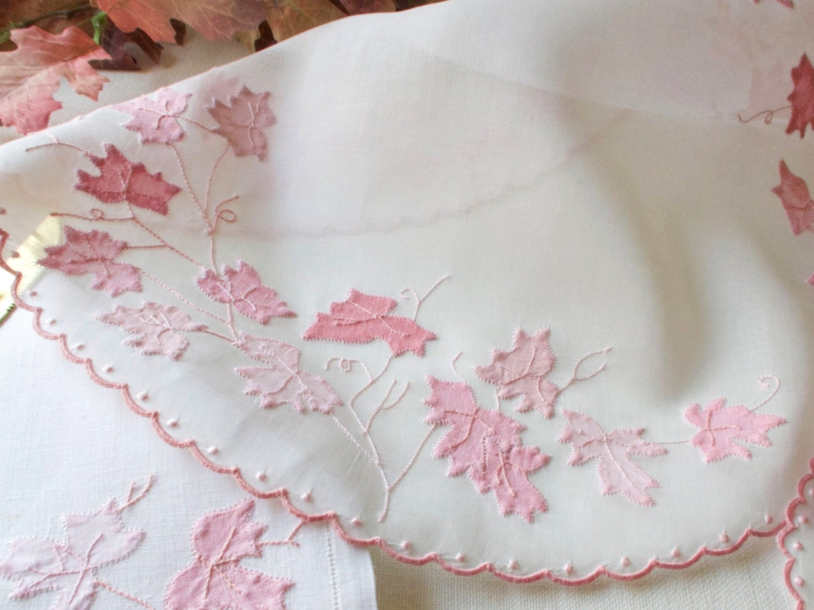 Close-up detail of vintage hand embroidered white organdy placemat border showing pink appliqué leaf vines ascalloped edged 