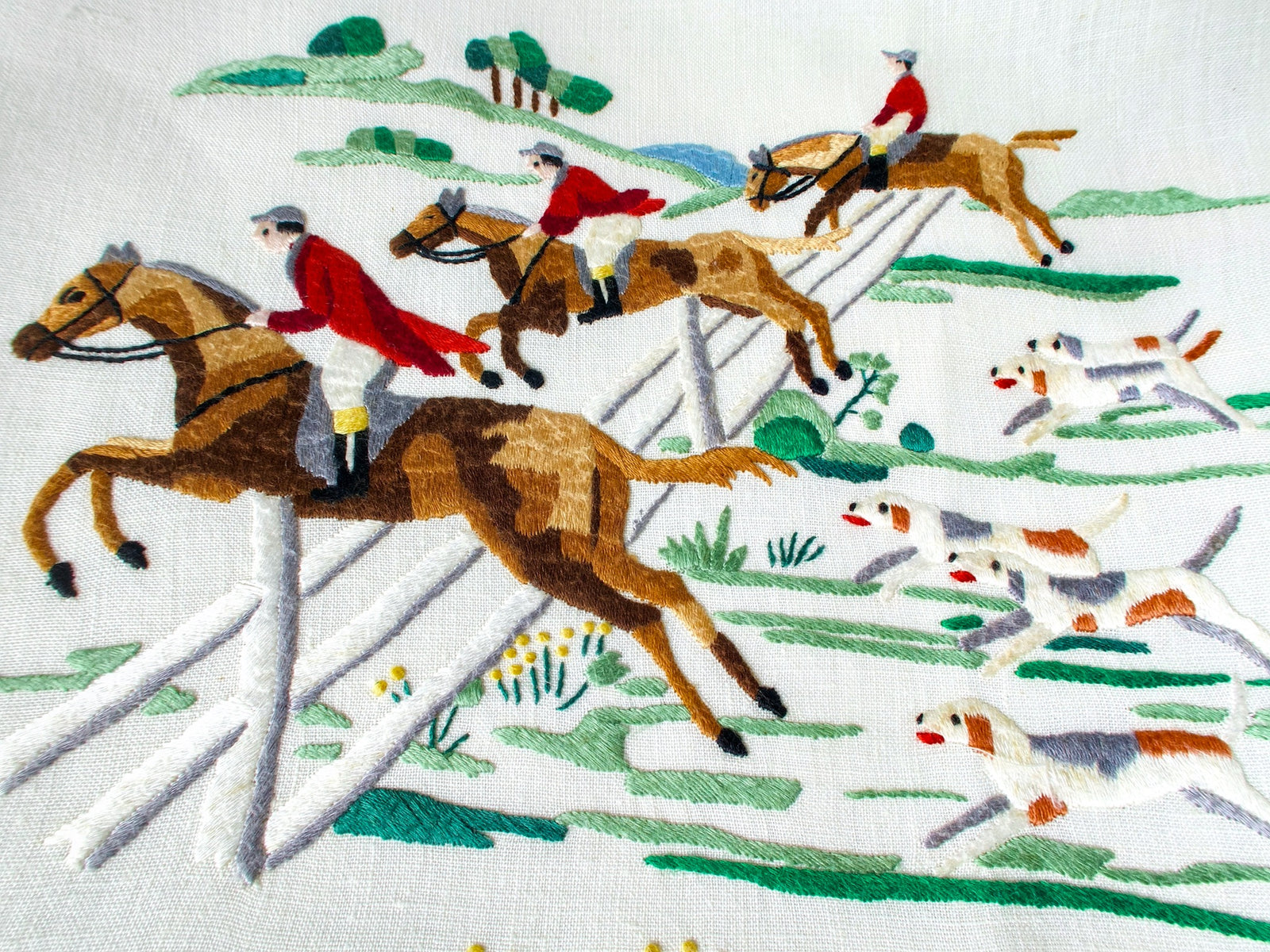 Vintage Madeira tablecloth with hand embroidered red-coated riders on galloping horses clearing a white fence, hounds racing below