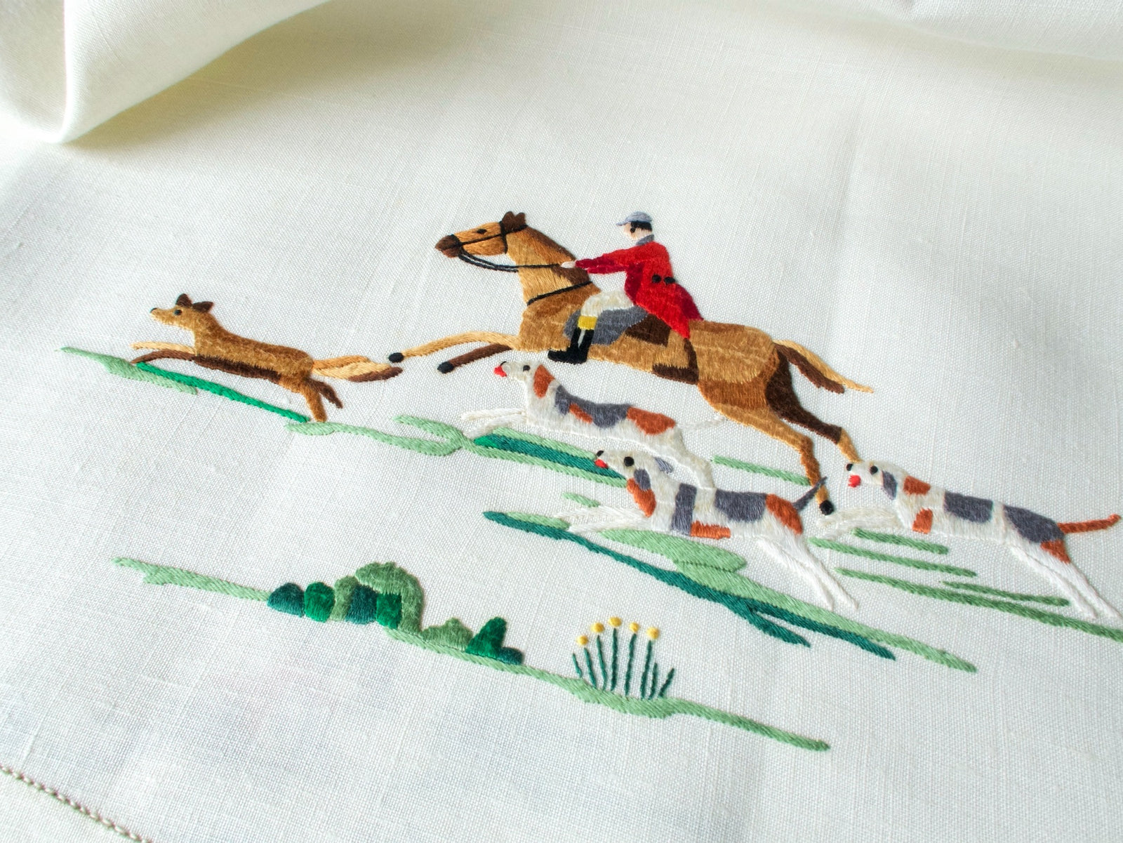 Hand embroidered fox racing ahead of a red-coated rider and three hounds on a vintage Madeira tablecloth